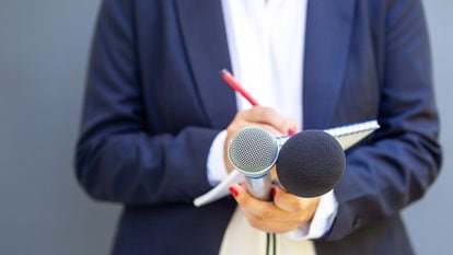 Una periodista toma apuntes y sostiene micrófonos durante una entrevista.