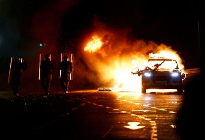 Agentes antidisturbios pasan cerca de un coche en llamas.