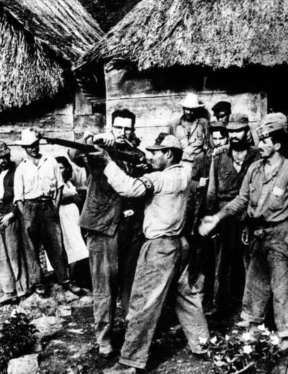 Fidel Castro, con un puro en los labios, instruye en el manejo de un arma a un guerrillero que se había unido a los combatientes de Sierra Maestra, varios de los cuales observan cómo aquel apunta con su arma con Fidel Castro al lado.
