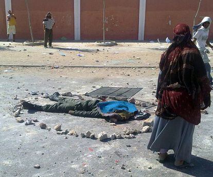 Varios saharauis contemplan el cuerpo sin vida de un agente antidisturbios marroquí en la avenida Smara de El Aaiún.