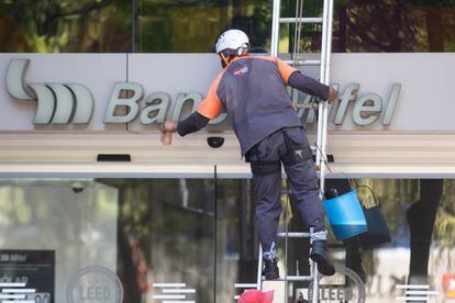 Un trabajador de limpieza asea la fachada de un banco.