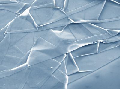 Lámina de grafeno arrugada que, vista al microscopio, se parece a tejido de seda dejado caer sobre una superficie (en este caso una oblea de silicio, visible en el extremo inferior derecho). La anchura de la imagen es de 20 micras.