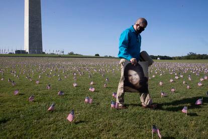 Un hombre cruza con un retrato de su madre, fallecida por covid, entre las miles de banderas colocadas junto a la base del obelisco de Washington como homenaje a las víctimas del coronavirus, el pasado 22 de septiembre.
