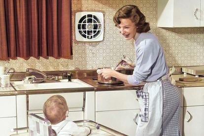 Una mujer cocina para su familia mientras cuida su hijo bebé en 1950.