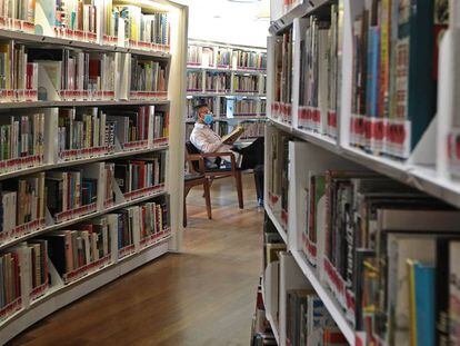 Un lector con mascarilla consulta un libro en una biblioteca de Singapur.