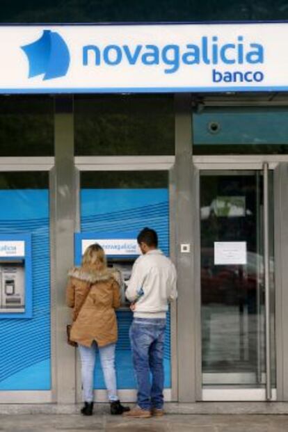 Dos jóvenes retiran dinero de un cajero en una sucursal de Novagalicia Banco.