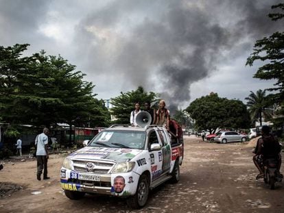 Un automóvil con propaganda electoral cerca de un incendio en un almacén de máquinas para votar, este jueves en Kinshasa.