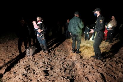 Un agente fronterizos lituano junto a migrantes detenidos cerca de la localidad de Vorzova tras llegar desde la vecina Bielorrusia este miércoles