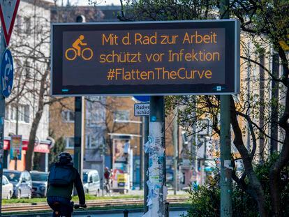 Un ciclista pasea junto a un cartel en Berlín en el que se anima a utilizar la bicicleta para aplanar la curva del coronavirus.