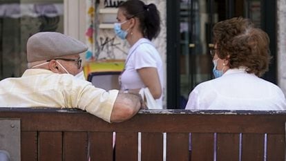 Una pareja de ancianos con mascarilla sentada en un banco en Madrid.