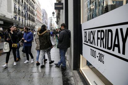 Varias personas pasan por delante de un cartel anunciando los descuentos del Black Friday en una tienda de la calle Preciados, en Madrid.