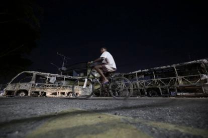 Un joven en bicicleta frente a dos de los autobuses incinerados, la noche del 23 de octubre.