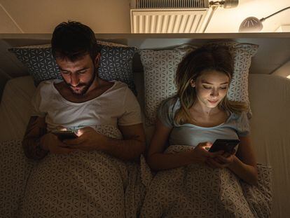 Una pareja consulta sus teléfonos móviles en la cama. Nueve de cada diez españoles usan las redes sociales y pasan casi dos horas al día en ellas.