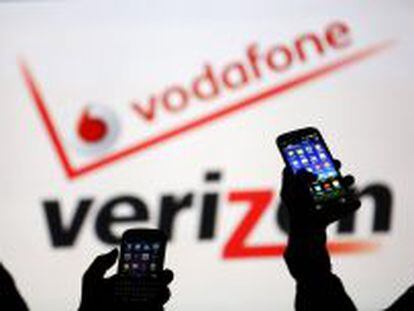 Dos usuarios manejan sus m&oacute;viles ante los logotipos de Vodafone y Verizon.