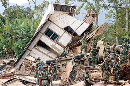 Un grupo de soldados indonesios busca supervientes bajo una casa arrancada de cuajo por las inundaciones.