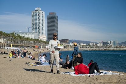 Un camarero lleva bebidas a las personas que disfrutan de las altas temperaturas en la playa de la Barceloneta, el pasado 25 de diciembre.
