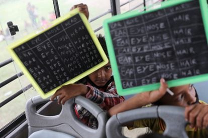 Dos estudiantes muestran sus tareas en la clase de inglés impartida en un bus de TejasAsia, una ONG que recorre los suburbios de Nueva Delhi para ofrecer educación.