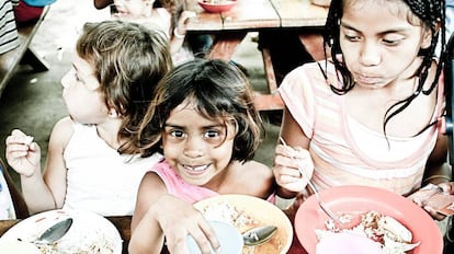 Unos niños huérfanos comen en una sala común.