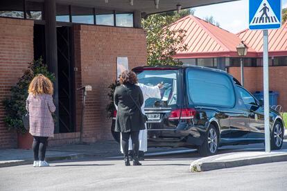 Un sacedorte bendice un féretro dentro de un coche fúnebre. 