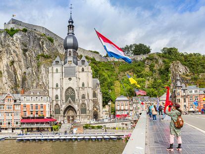 Turistas cruzando el puente Charles de Gaulle mientras fotografían la colegiata de Dinant (Bélgica).