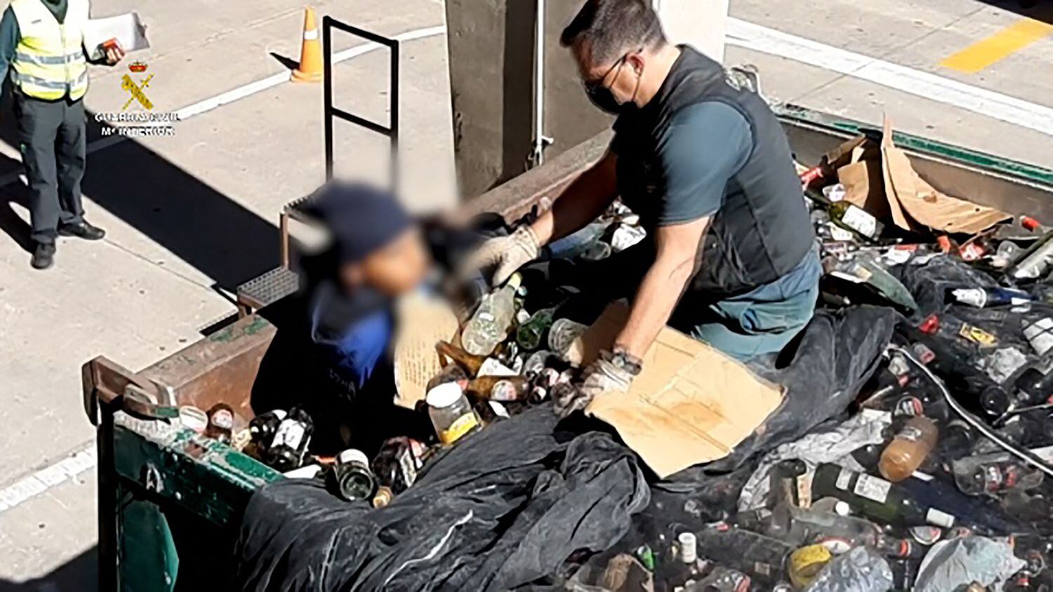Un agente de la Guardia Civil recata a un migrante entro de un contenedor lleno de fragmentos de vidrio reciclado en el puerto de Melilla.
