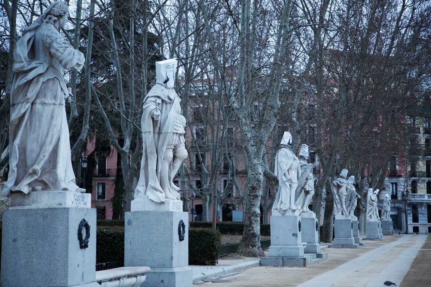 Las estatuas de personajes históricos masculinos de la plaza de Oriente de Madrid, tapadas con bolsas con rostros femeninos, este lunes. CARANTONIA 