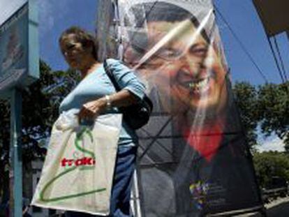 Una mujer camina frente a un poster de Hugo Chávez