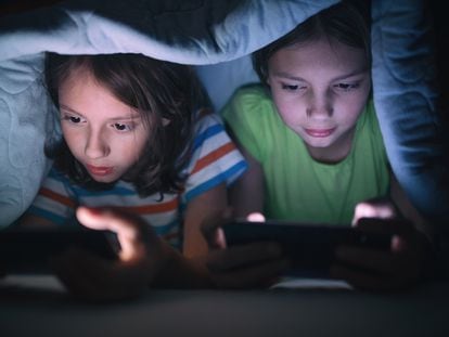 Un niño y una niña usan sus dispositivos electrónicos bajo las sábanas.