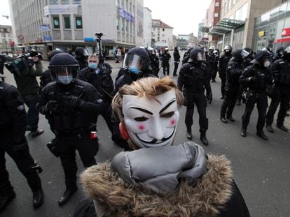 Un manifestante con una máscara de Guy Fawkes se coloca delante de los agentes de policía en Kassel (Alemania), este sábado.