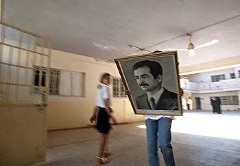 Una niña lleva un retrato de Sadam Husein a un almacén tras ser descolgado de su aula en una escuela de Bagdad.