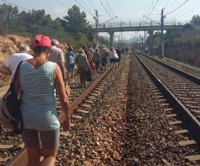 Pasajeros de un tren afectado caminan por las vías.