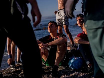 Un grupo de menores migrantes, sentados en la playa tras llegar a nado a Ceuta, espera en la arena rodeados de dos agentes de la Guardia Civil, el 19 de mayo.