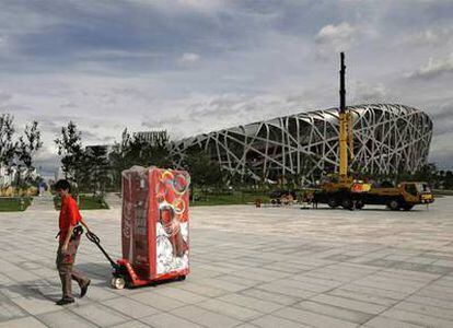 Un trabajador traslada una máquina de Coca Cola junto al estadio olímpico.
