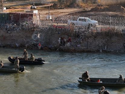 Un grupo de migrantes en el borde del río Bravo a la altura de Eagle Pass, mientras pasan lanchas de la Guardia Nacional de Texas, el 3 de febrero.