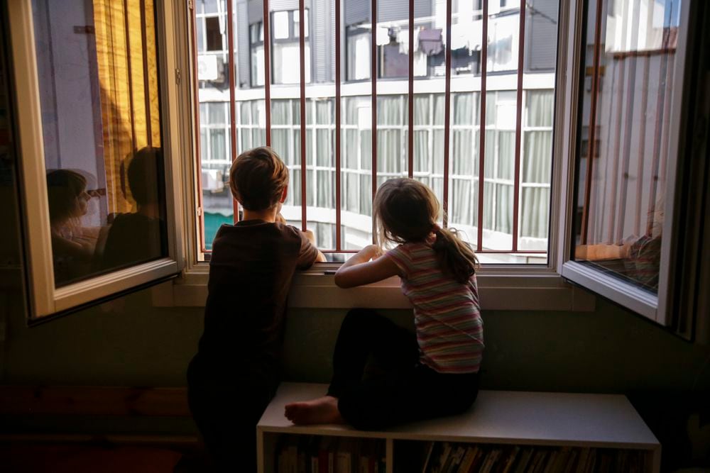 Dos hermanos miran por la ventana de su dormitorio durante el confinamiento en Madrid.