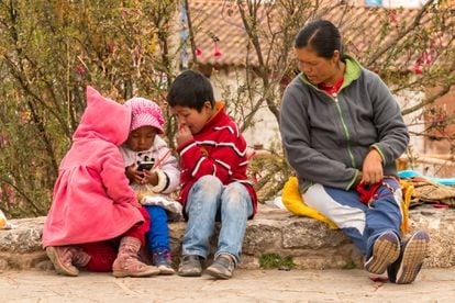 Una mujer indígena vigila a sus hijos que juegan con un teléfono móvil en Chinchero, Perú