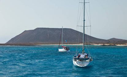 Barco fondeados frente a la playa de La Concha, en islote de Lobos (Fuerteventura), con el volcán de La Caldera recortado al fondo.