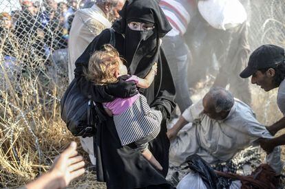 Una mujer siria que huye de la guerra lleva a su hijo mientras ella pasa a través de vallas fronterizas para entrar en territorio turco.