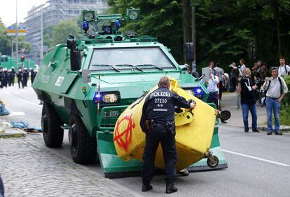 Un oficial de policía retira un contenedor de basura dejado por los manifestantes frente a un vehículo policial.  