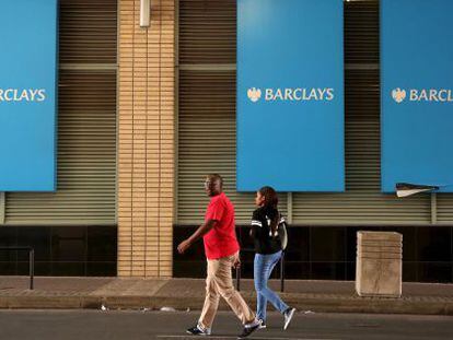Dos personas pasan por delante de tres logos de Barclays y Johannesburgo (Sud&aacute;frica).
