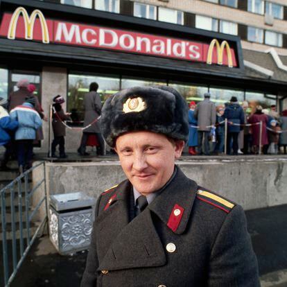 Un policía soviético sonríe a la cámara mientras, al fondo, se organiza una cola de horas para probar una hamburguesa en el primer día que abrió McDonalds en Moscú, el 31 de enero de 1990.