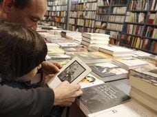 Dos lectores consultan un libro digital en una librería tradicional.