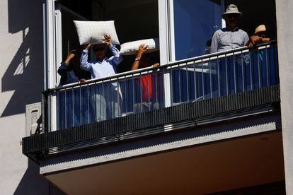 Varios vecinos se protegen del sol en una terraza mientras siguen el mitin del PP en Madrid. 