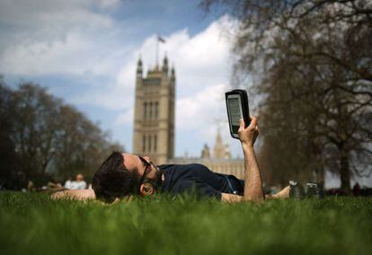 Un hombre lee un libro electrónico en un parque de Londres.