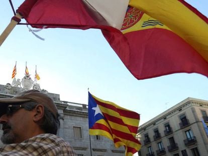 Un hombre porta una bandera de Espa&ntilde;a mientras ondea otra independentista de catalu&ntilde;a al fondo.