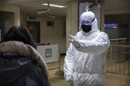 Un trabajador con un traje de materiales peligrosos le hace un gesto a un pasajero en una estación de metro en Beijing.