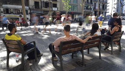 Varias personas sentadas en los bancos de La Rambla.
