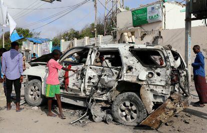 Civiles se encuentran cerca de los restos de un automóvil destruido en un ataque armado en el Hotel Elite, en la playa de Lido, en Mogadiscio, capital de Somalia, el 17 de agosto de 2020. 