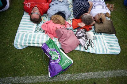 Varias personas descansan durante la larga espera horas antes de la apertura de las puertas del Club de Tenis de Wimbledon donde se celebra el torneo.