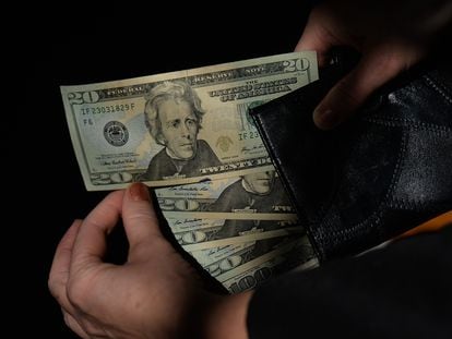 Persona sostiene un fajo de billetes de dólares estadounidenses.